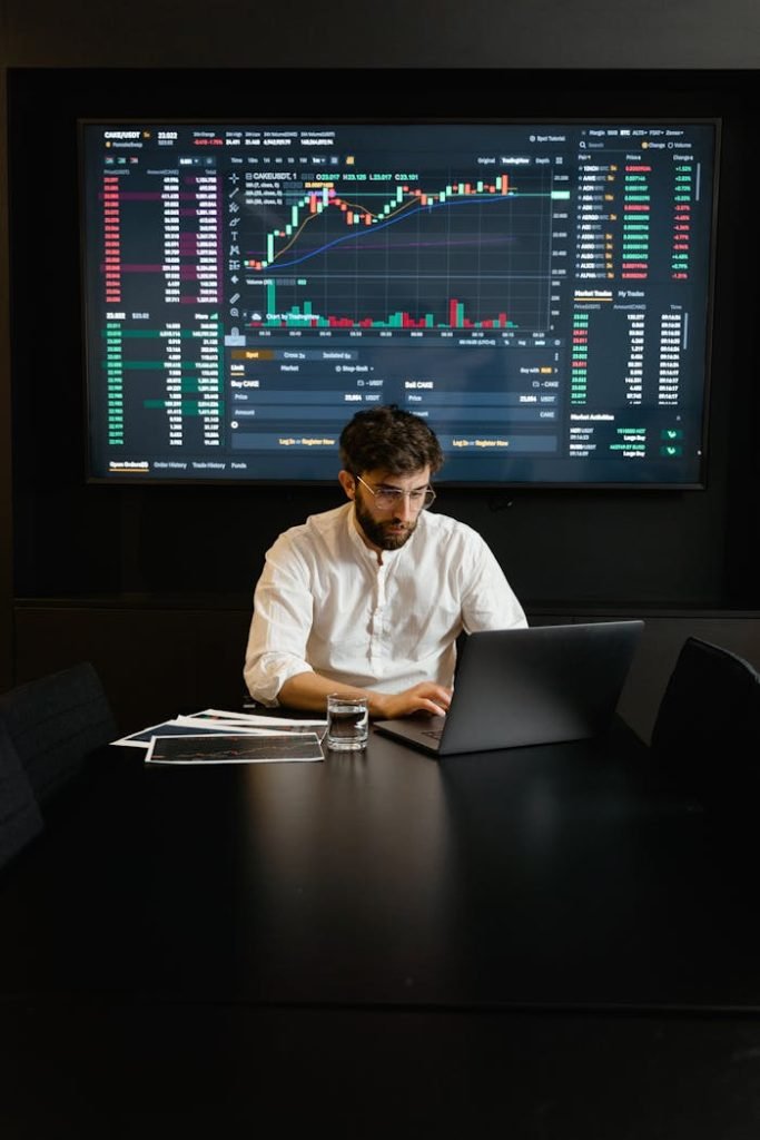 focused-professional-man-using-laptop-7567529 A focused man analyzing stock market trends on a laptop in an office setting with charts displayed.