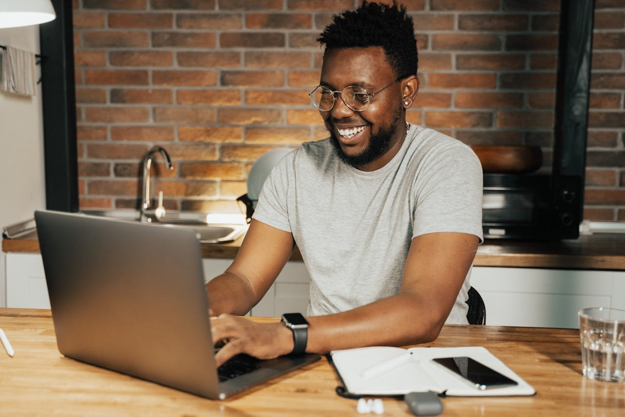 About African American man smiling while working remotely on laptop from home office